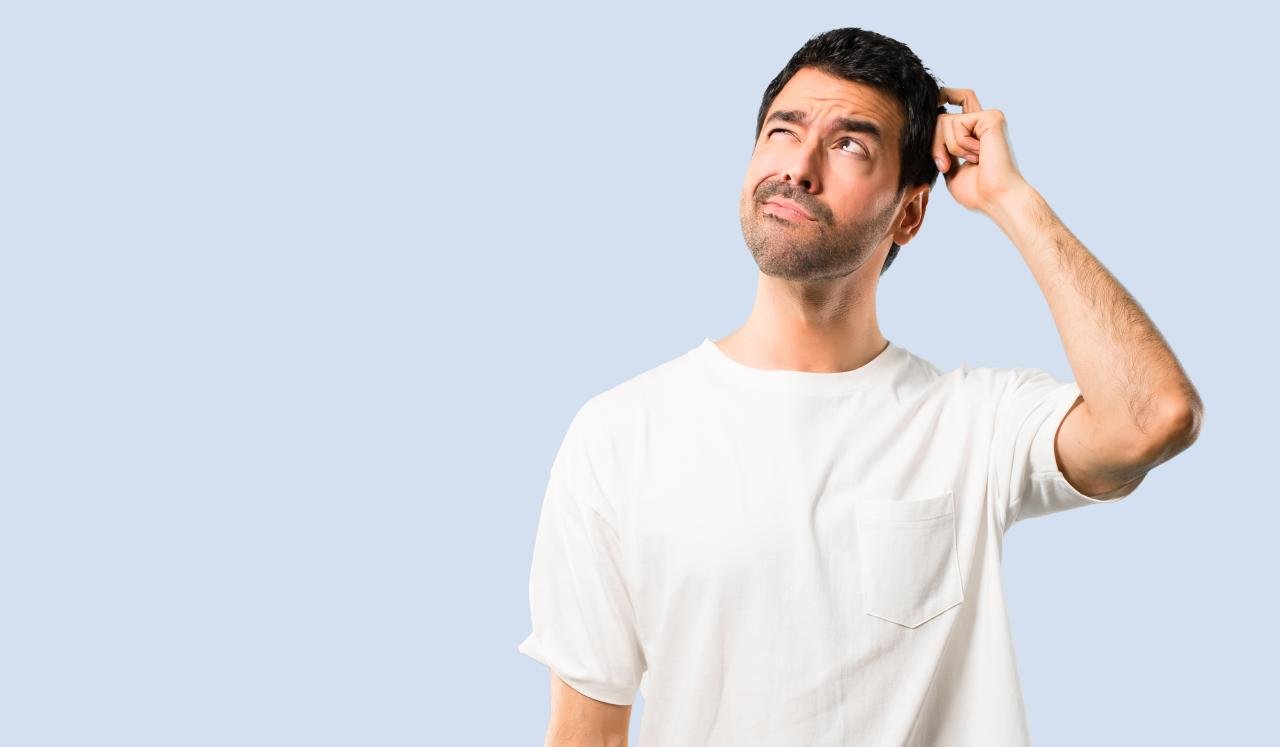 A man in a white shirt scratching his head | Source: Shutterstock