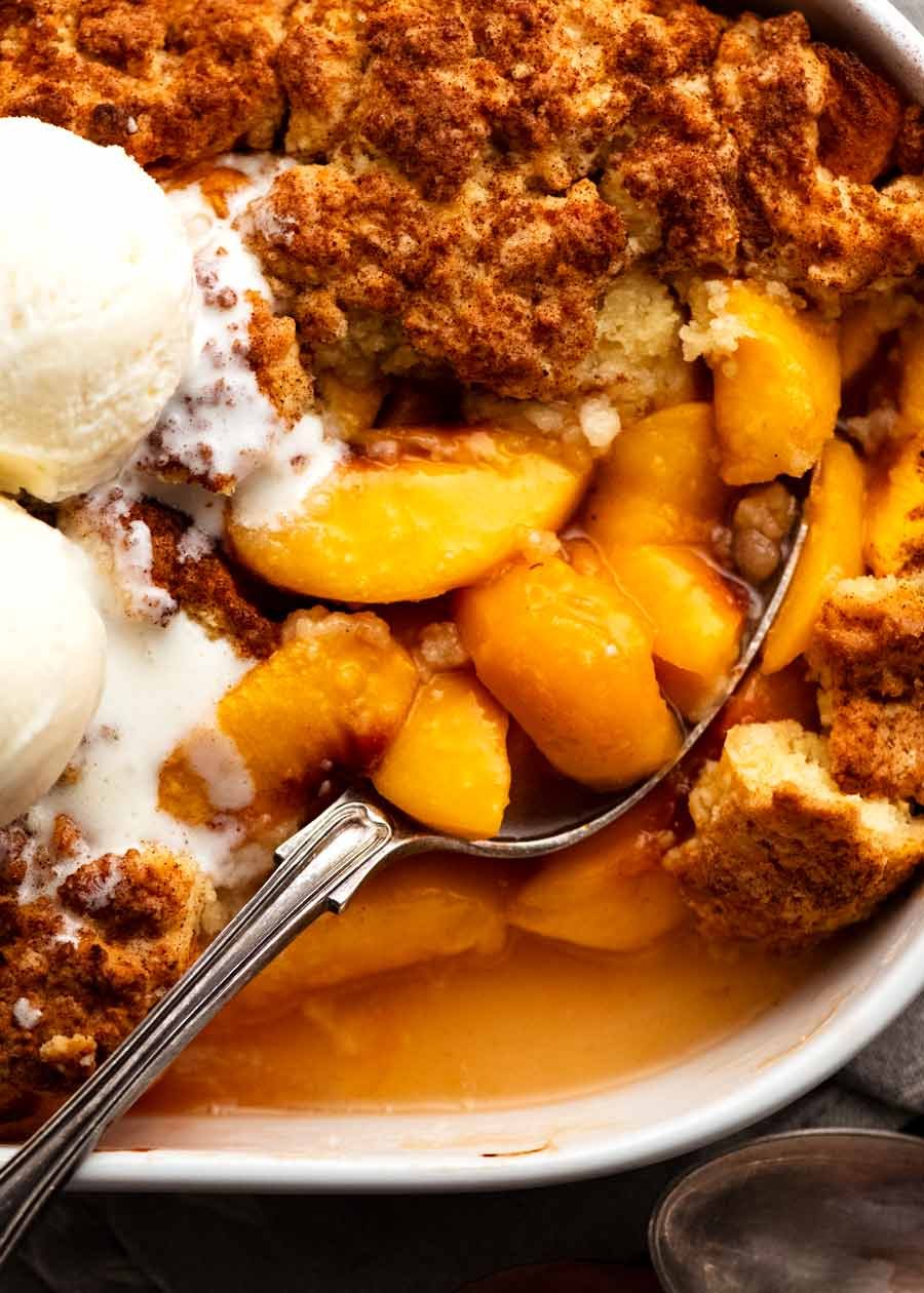 Close up scooping peaches out of Peach Cobbler in baking dish