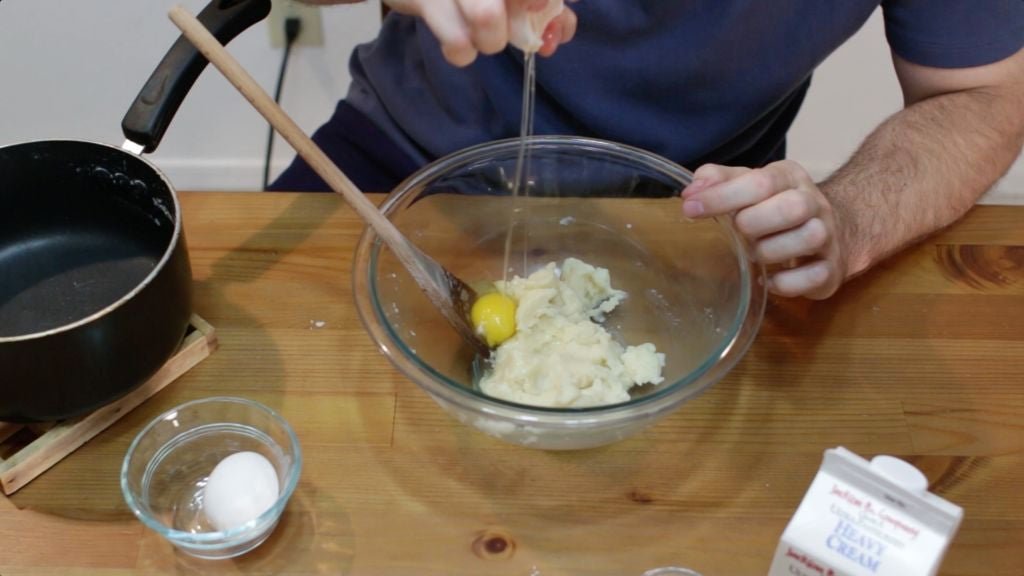 Eggs being cracked and dropped into cream puffs dough.