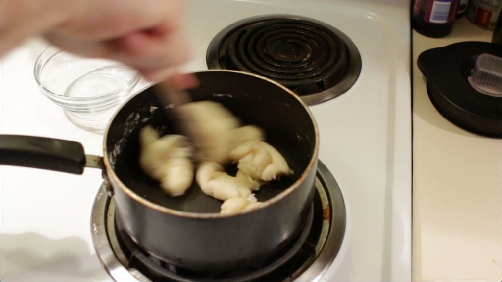 Easy cream puff dough coming together in a pot as a hand stirs it with a wooden spoon