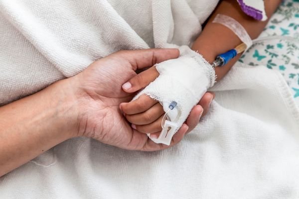 Mother holding child's hand who have IV solution in the hospital